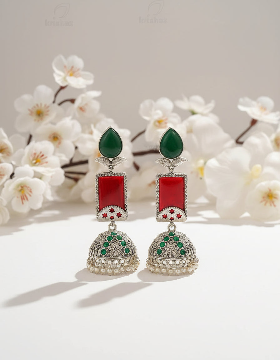 Ornate earrings with red and green stones on a branch against a beige background