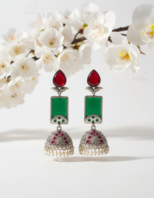 Ornate earrings with red, green, and pearl details on a branch against a brown background