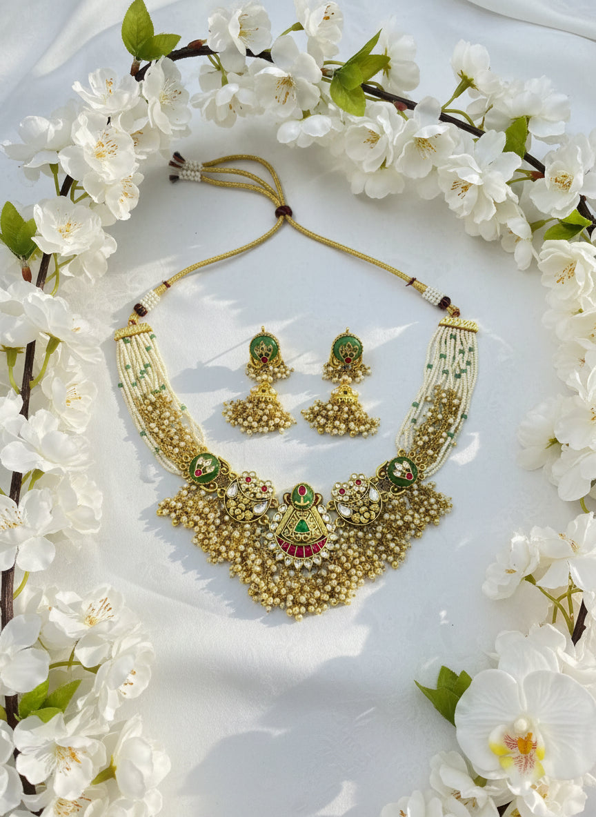 Gold necklace with green and red accents on a white surface with a pink background