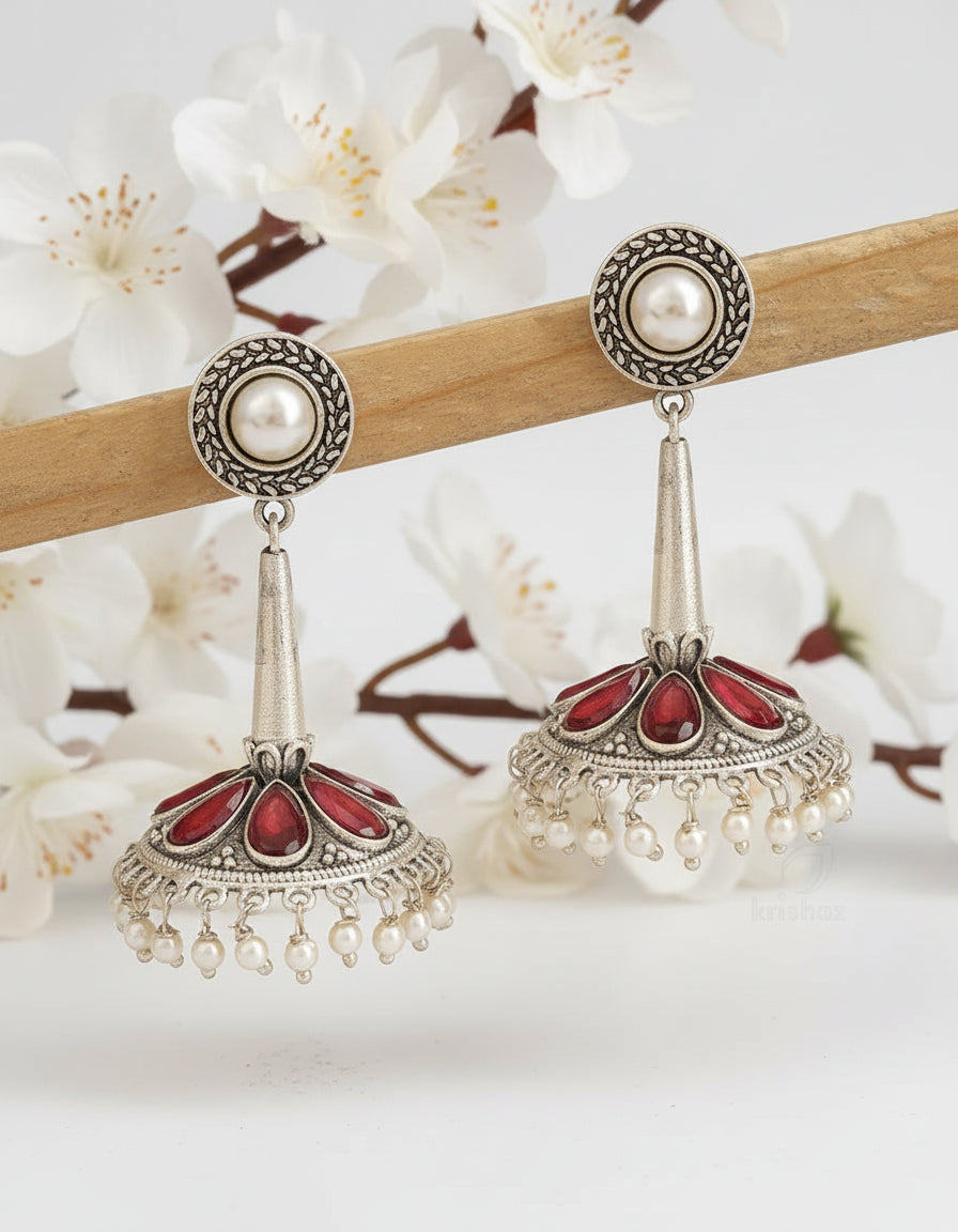 Ornate silver earrings with red and pearl accents on a brown background