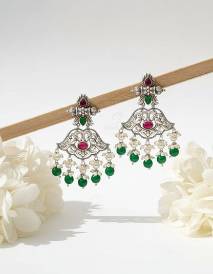 Ornate silver earrings with green and red stones on a wooden stick