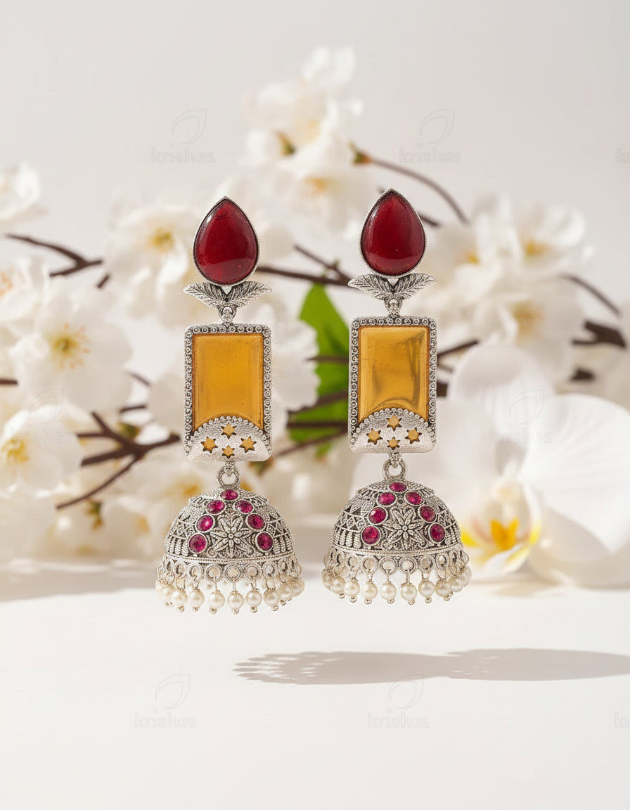 Ornate earrings with red and yellow stones on a branch against a brown background