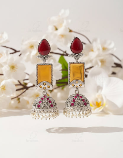 Ornate earrings with red and yellow stones on a branch against a brown background