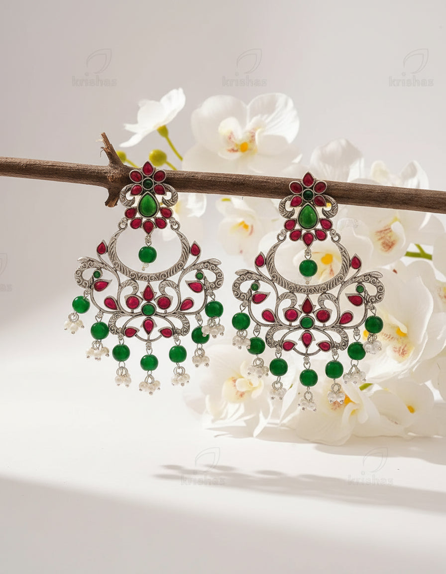Ornate earrings with green and red stones on a brown background