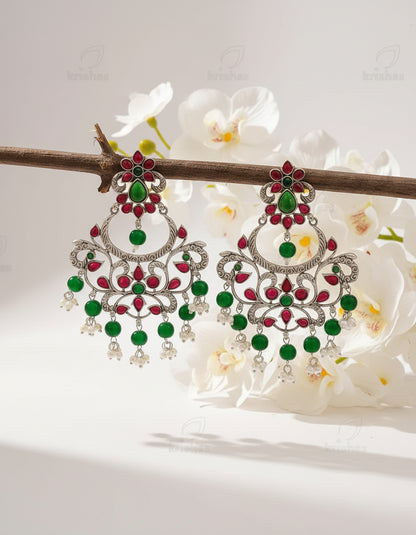 Ornate earrings with green and red stones on a brown background