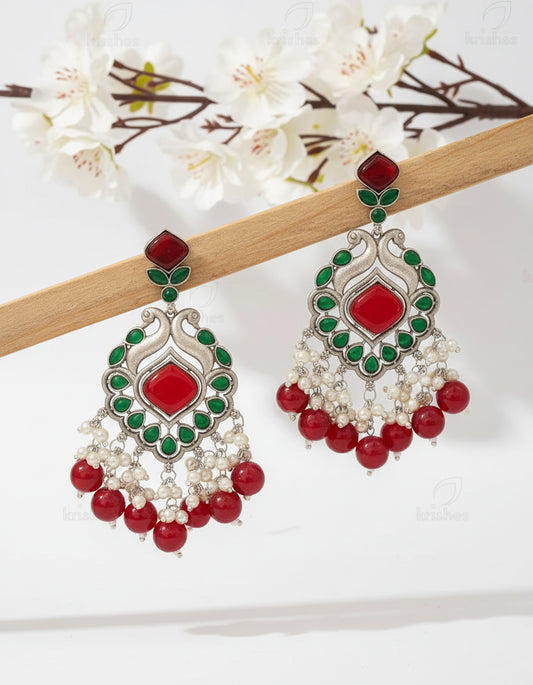 Ornate earrings with red, green, and pearl details on a brown background