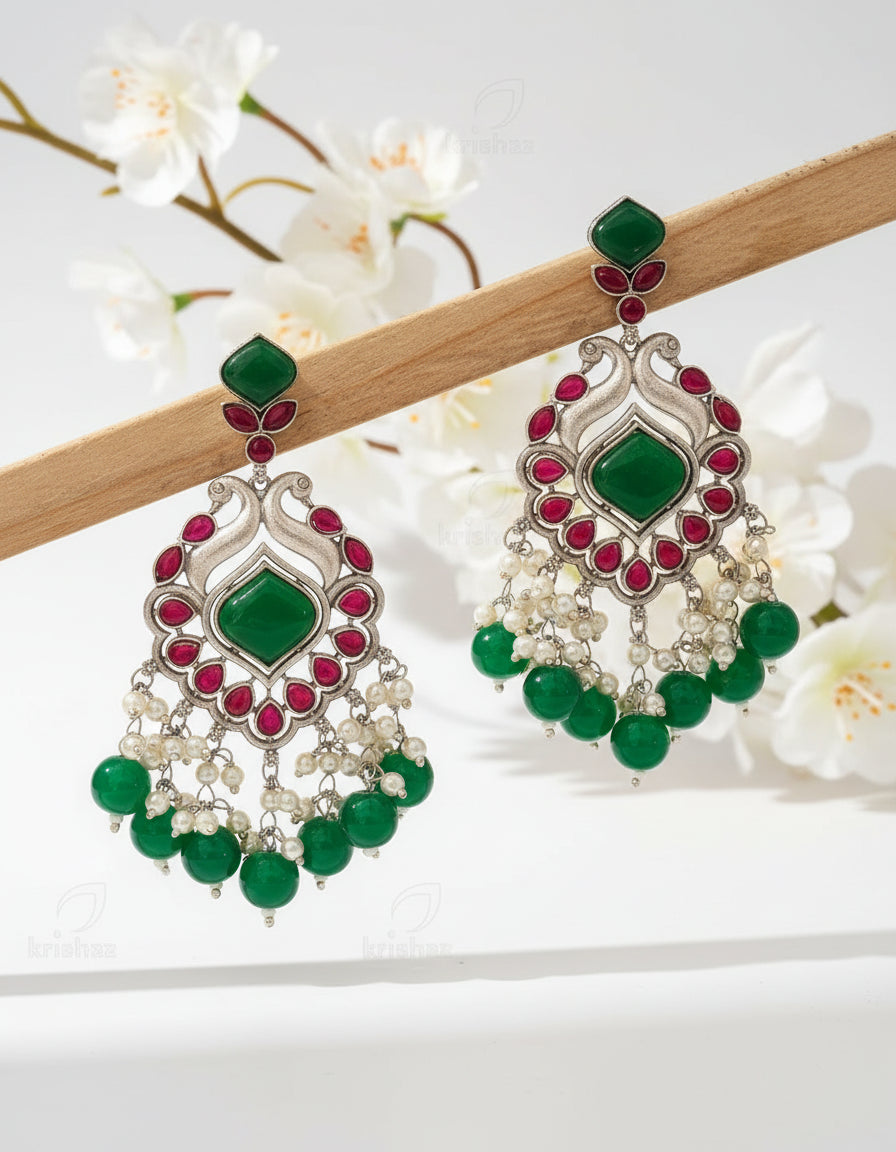 Ornate earrings with green stones and pearls on a brown background