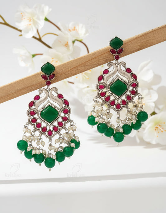 Ornate earrings with green stones and pearls on a brown background