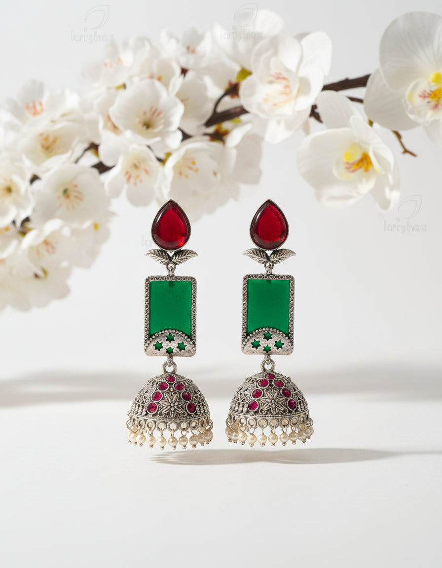 Ornate earrings with red, green, and pearl details on a branch against a brown background