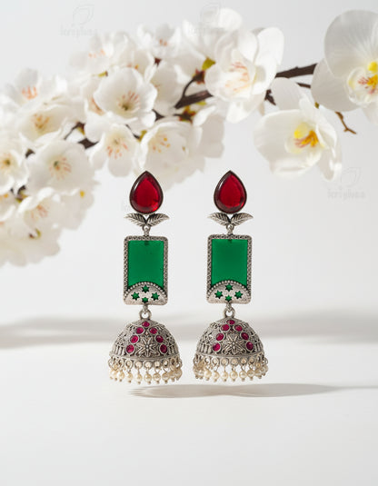 Ornate earrings with red, green, and pearl details on a branch against a brown background
