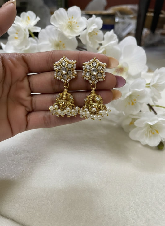 Gold earrings with intricate designs held by a hand against a blurred floral background