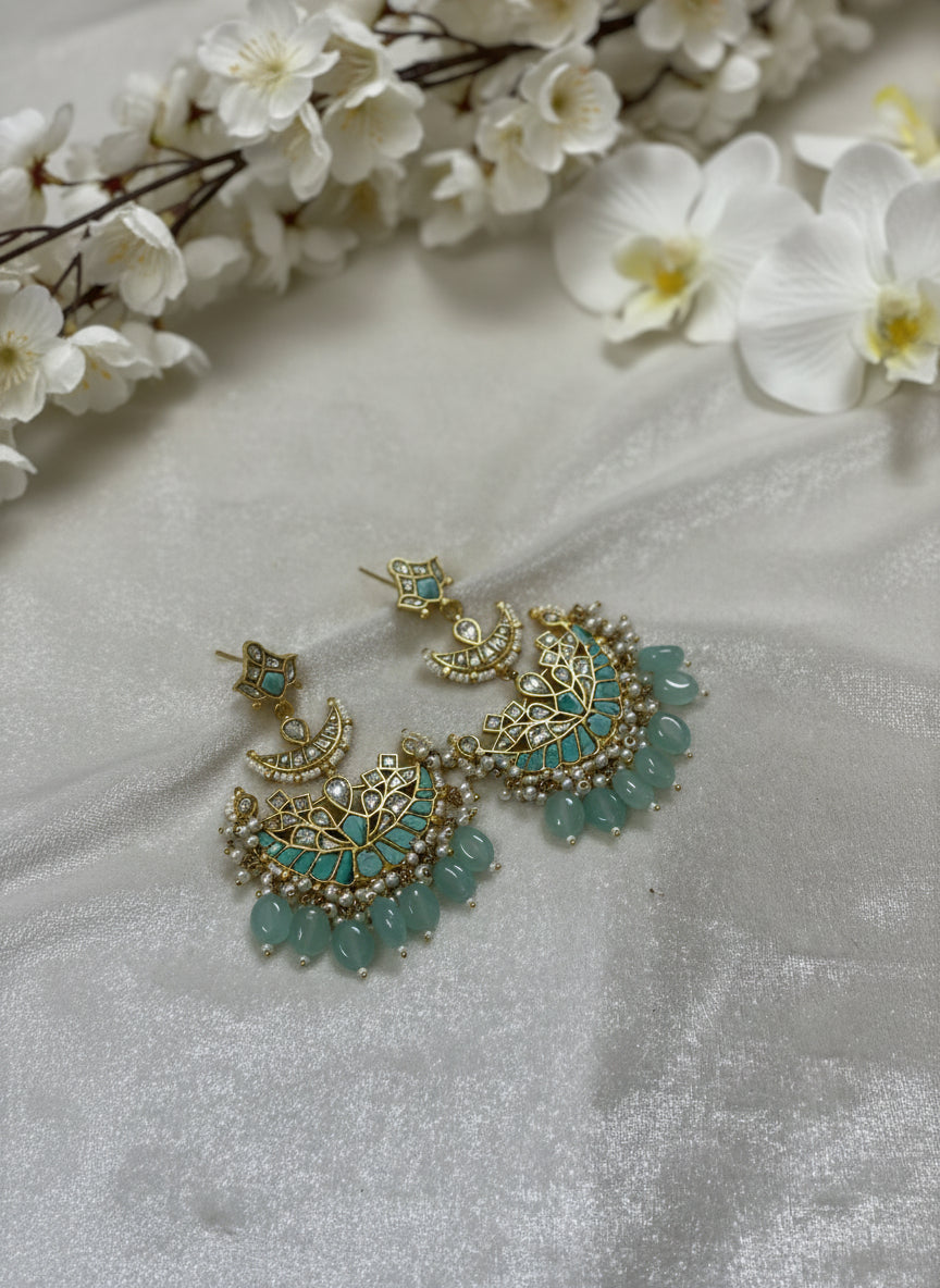 Decorative earrings with gold and turquoise details on a white fabric background with flowers.