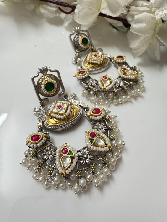 Ornate silver and gold earrings with gemstones on a white surface with flowers.