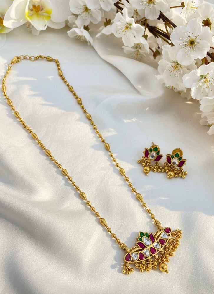 Gold necklace with gemstones on a pink and white background