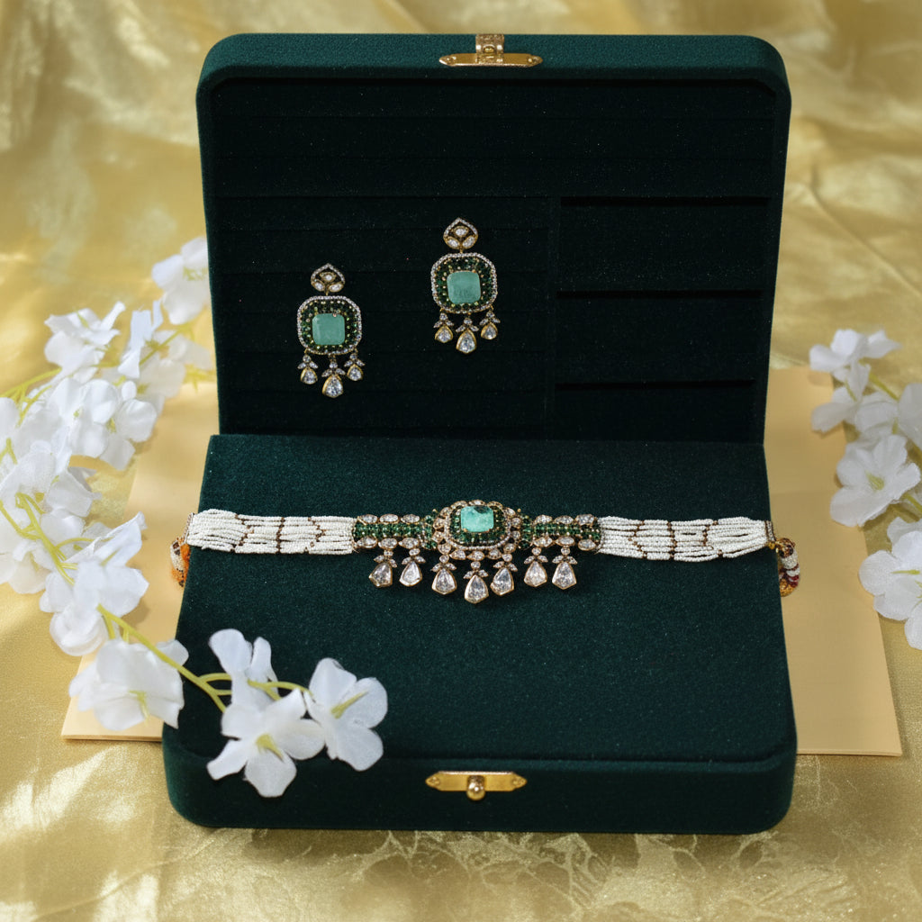 Jewelry set with earrings and a necklace on a dark green stand with white flowers in the background.