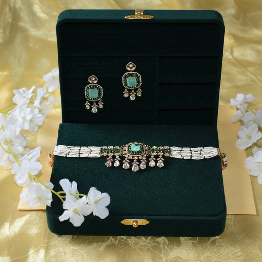 Jewelry set with earrings and a necklace on a dark green stand with white flowers in the background.