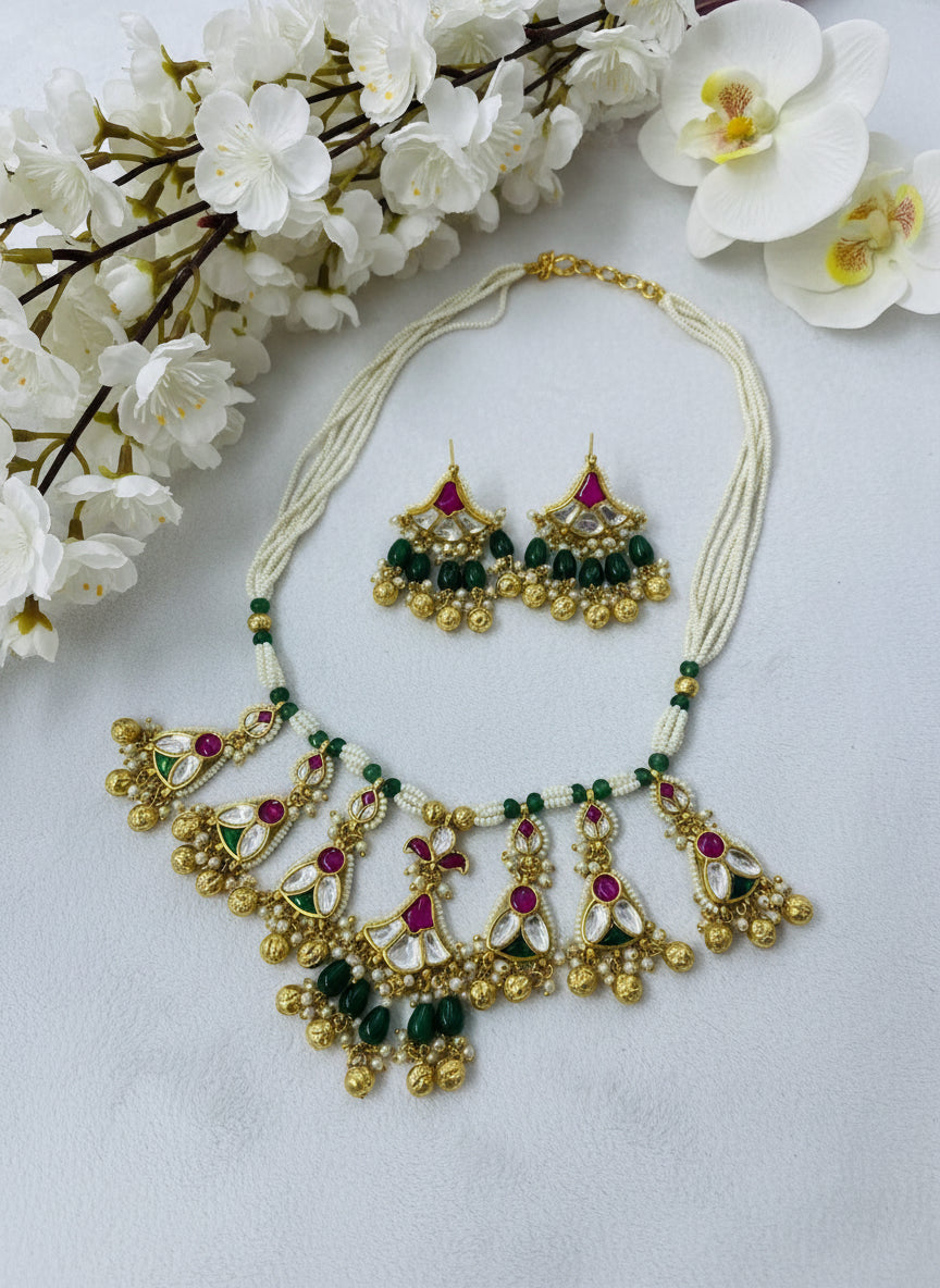 Gold necklace with green and red stones on a white and pink background