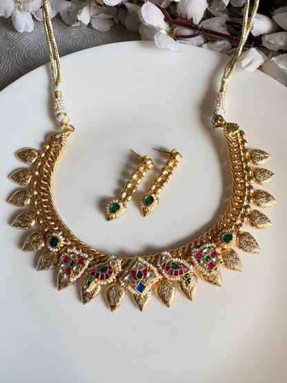 Gold necklace and earrings with gemstones on a white plate with flowers in the background