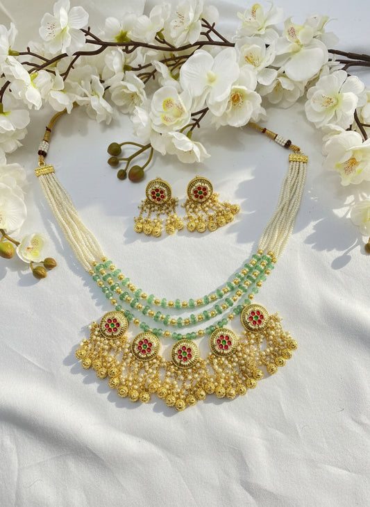 Gold necklace with green beads on a pink fabric background