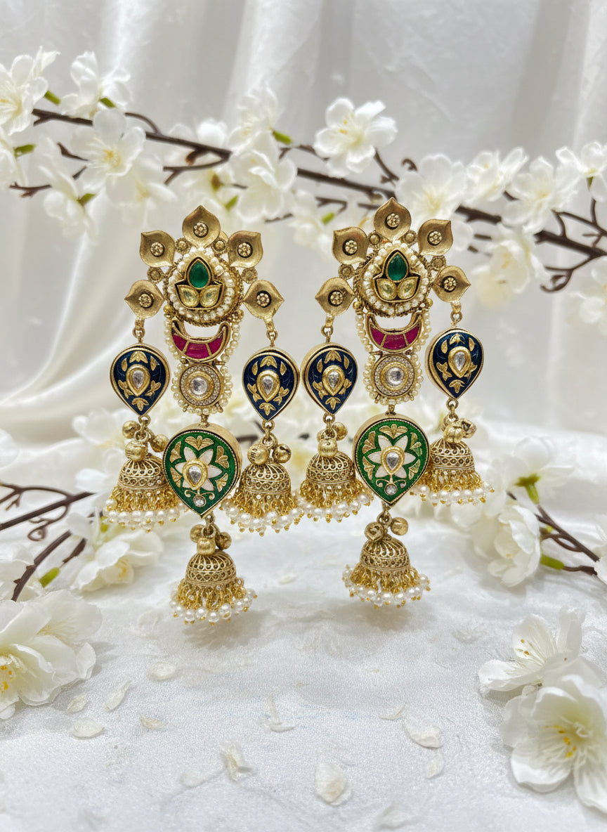 Gold and green decorative earrings held by a hand with a blurred indoor background.