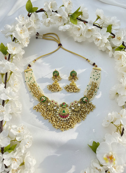 Gold necklace with green and red accents on a white surface with a pink background