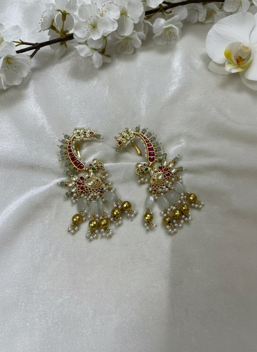 Ornate gold earrings with red and green gemstones on a white fabric background