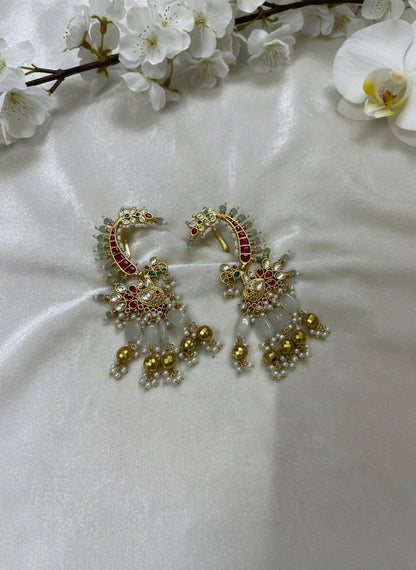 Ornate gold earrings with red and green gemstones on a white fabric background