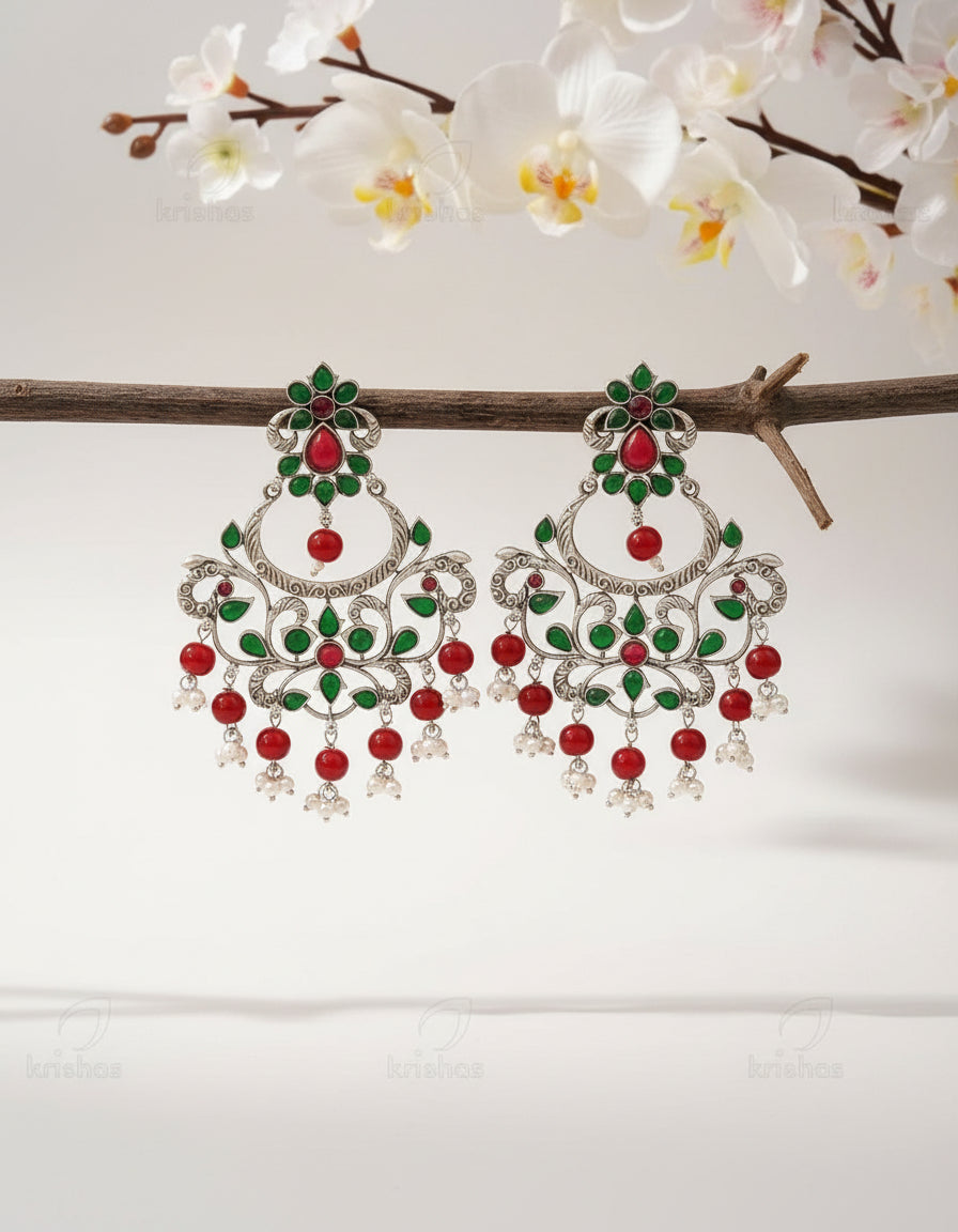 Pair of ornate earrings with red and green stones on a wooden branch.