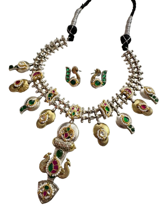 Ornate necklace with peacock designs and matching earrings on a white surface.