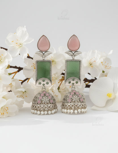 Decorative earrings with green and pink stones on a wooden branch